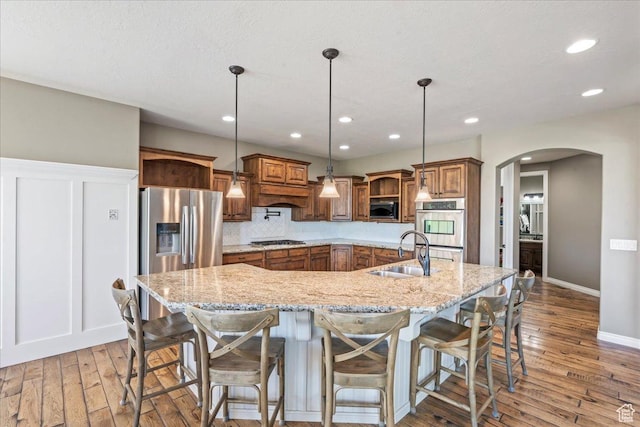 916 Country Ln, Farmington, UT 84025 - kitchen with appliances with stainless steel finishes, a sink, brown cabinets, arched walkways, and light wood-type flooring