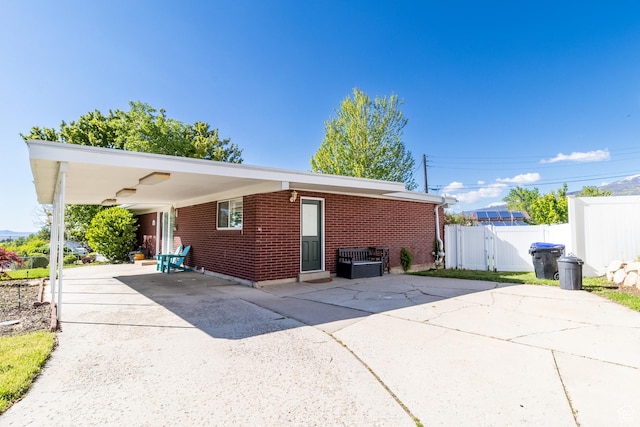 rear view of house featuring driveway, brick siding, fence, and a carport