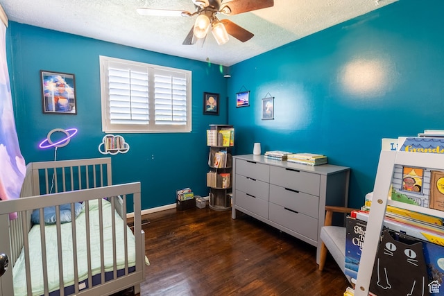 bedroom featuring a textured ceiling, a crib, wood finished floors, ceiling fan, and baseboards