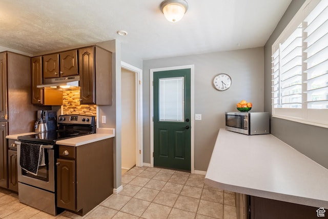 kitchen featuring appliances with stainless steel finishes, under cabinet range hood, light countertops, tasteful backsplash, and light tile patterned floors