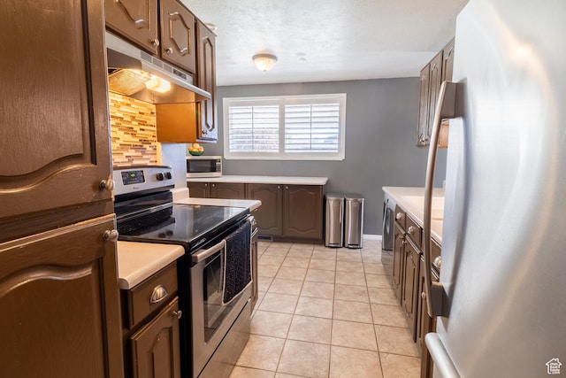 kitchen with appliances with stainless steel finishes, under cabinet range hood, light countertops, decorative backsplash, and light tile patterned flooring