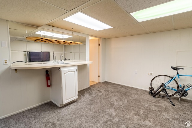 kitchen with a sink, carpet, a paneled ceiling, light countertops, and baseboards