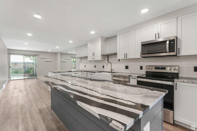 kitchen featuring stainless steel appliances, a sink, tasteful backsplash, light wood-type flooring, and white cabinets