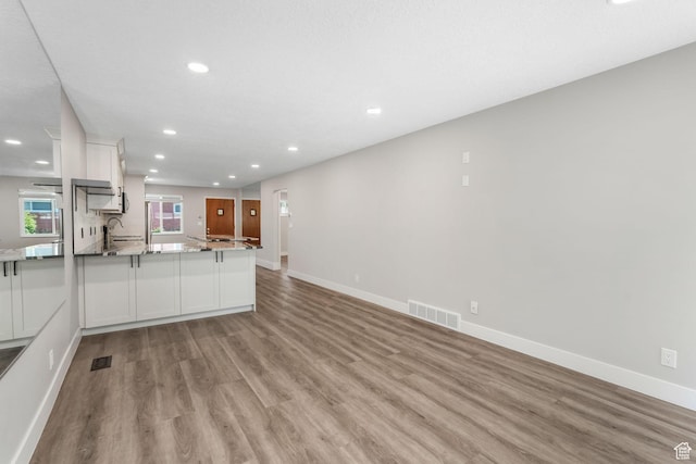 unfurnished living room with recessed lighting, light wood-style flooring, baseboards, and a sink