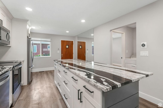 kitchen with stainless steel appliances, light wood finished floors, baseboards, a kitchen island, and white cabinets