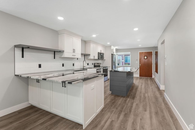 kitchen featuring appliances with stainless steel finishes, wood finished floors, white cabinetry, decorative backsplash, and baseboards
