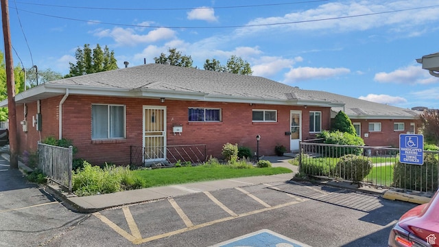 view of front of property featuring brick siding, fence, a shingled roof, and uncovered parking