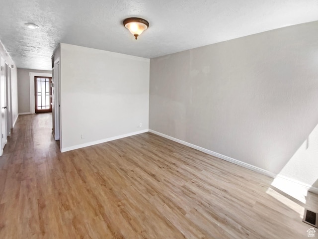spare room featuring light wood-style flooring, baseboards, and a textured ceiling