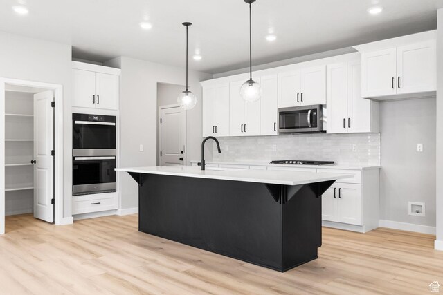kitchen featuring stainless steel microwave, double wall oven, a sink, light wood finished floors, and backsplash