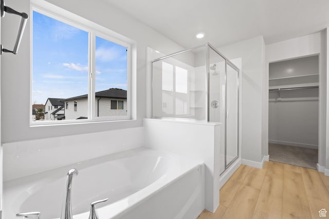 bathroom featuring a stall shower, a garden tub, a walk in closet, wood finished floors, and recessed lighting