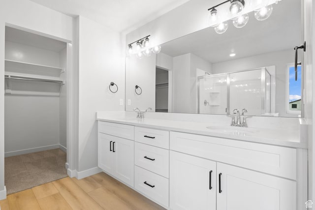 full bath with a stall shower, a spacious closet, double vanity, wood finished floors, and baseboards