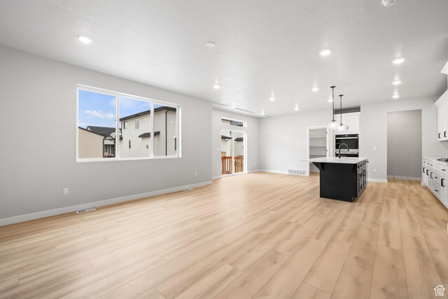 kitchen featuring an island with sink, light wood finished floors, open floor plan, light countertops, and recessed lighting