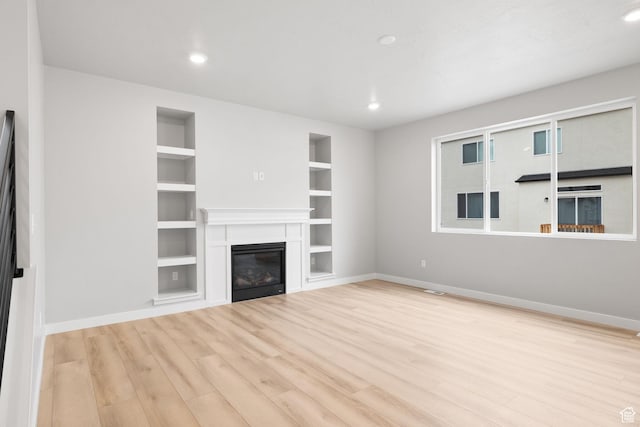 unfurnished living room featuring built in features, wood finished floors, baseboards, a glass covered fireplace, and recessed lighting