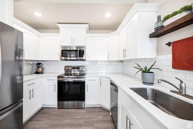 kitchen with appliances with stainless steel finishes, a sink, light countertops, white cabinets, and recessed lighting