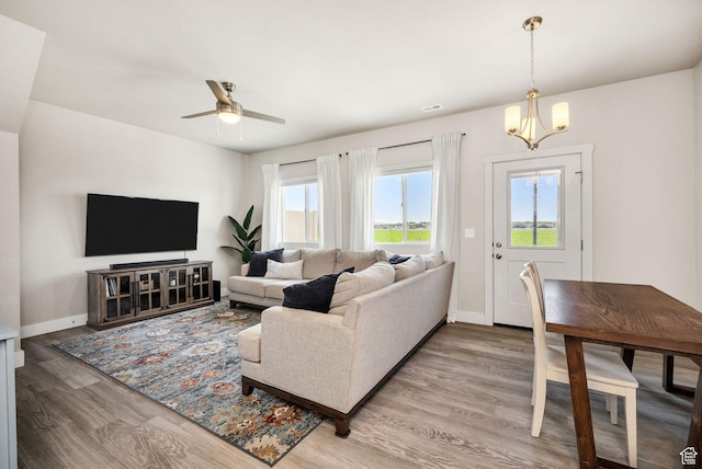 living area with light wood-style floors, a chandelier, ceiling fan, and baseboards
