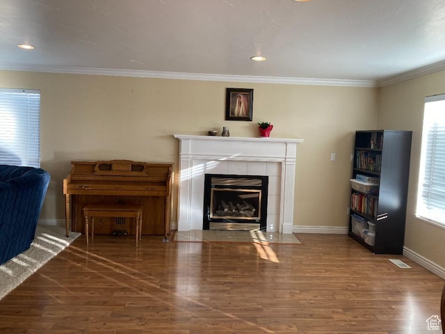 living area with wood finished floors, a fireplace, plenty of natural light, baseboards, and ornamental molding