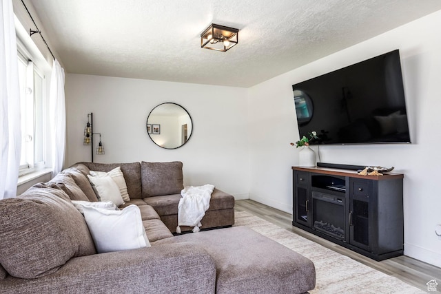 living room with light wood-type flooring, baseboards, and a textured ceiling
