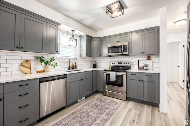 kitchen with stainless steel appliances, a sink, gray cabinets, light wood finished floors, and light countertops