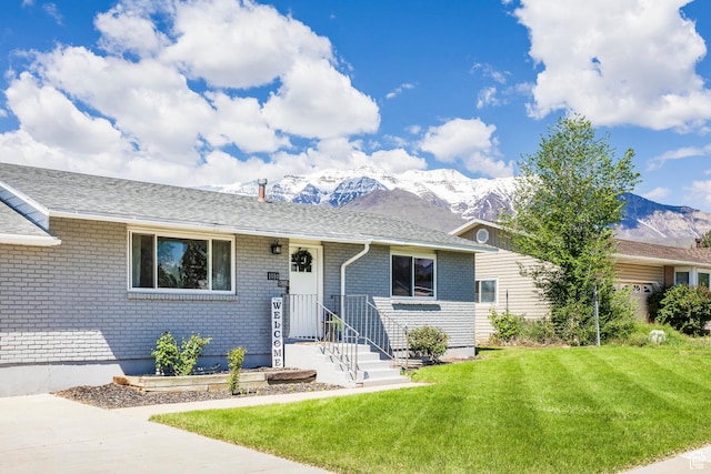 single story home featuring a mountain view, a front lawn, brick siding, and a shingled roof