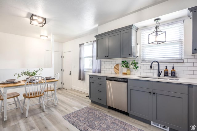 kitchen with stainless steel dishwasher, a sink, gray cabinets, tasteful backsplash, and light countertops
