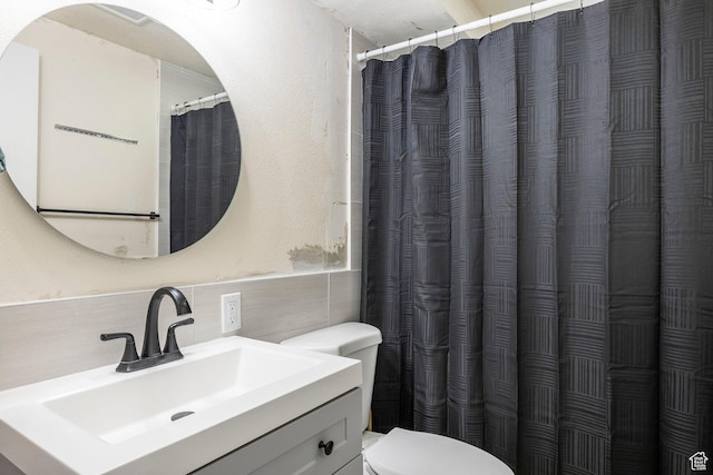 full bath featuring tile walls, toilet, vanity, and a wainscoted wall