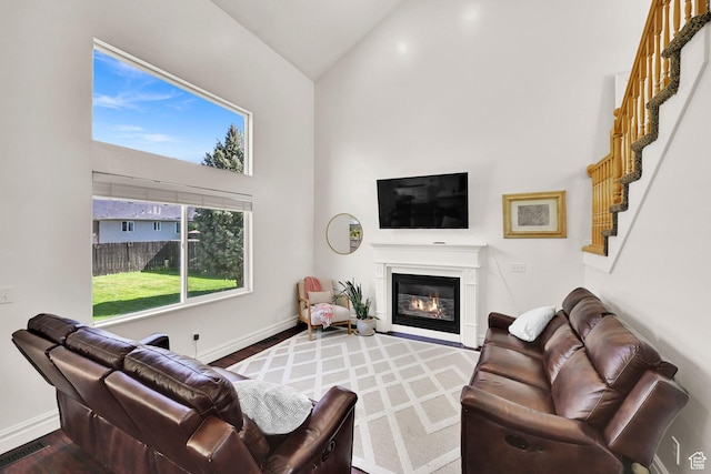 living room with high vaulted ceiling, wood finished floors, a glass covered fireplace, stairway, and baseboards