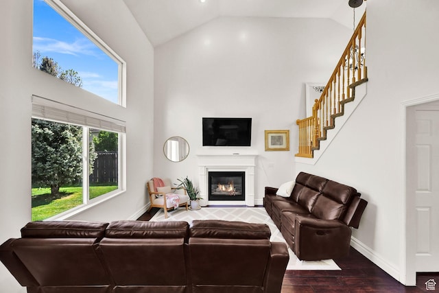 living room featuring high vaulted ceiling, wood finished floors, stairs, a glass covered fireplace, and baseboards