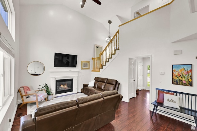 living room with ceiling fan, a glass covered fireplace, high vaulted ceiling, dark wood-type flooring, and stairs