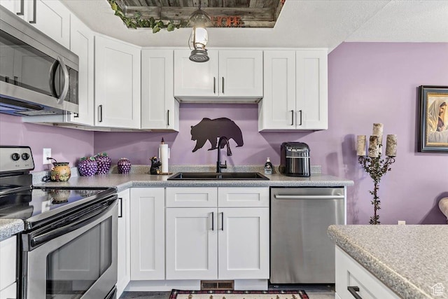 kitchen with stainless steel appliances, a sink, white cabinetry, and light countertops