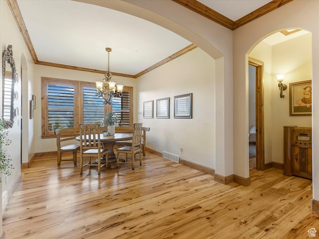 dining room with light wood-style flooring, arched walkways, a chandelier, ornamental molding, and baseboards