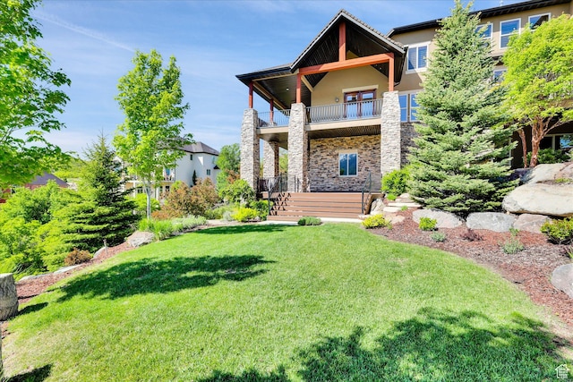 rear view of property featuring stone siding, a balcony, a lawn, and stucco siding