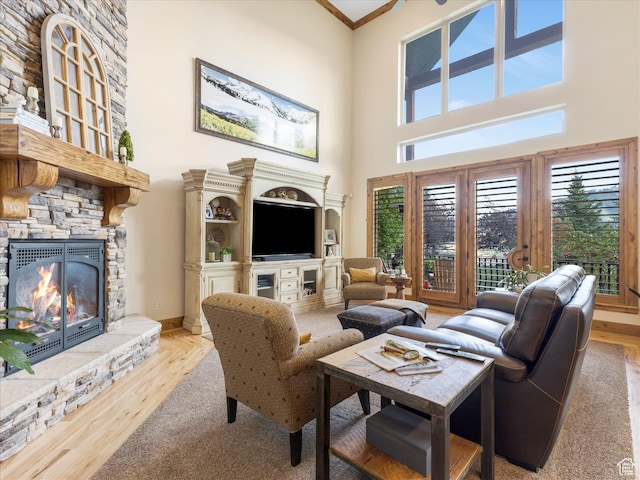 living room featuring a stone fireplace, a high ceiling, crown molding, and wood finished floors