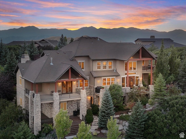 rear view of house with a balcony, stone siding, stucco siding, and a mountain view