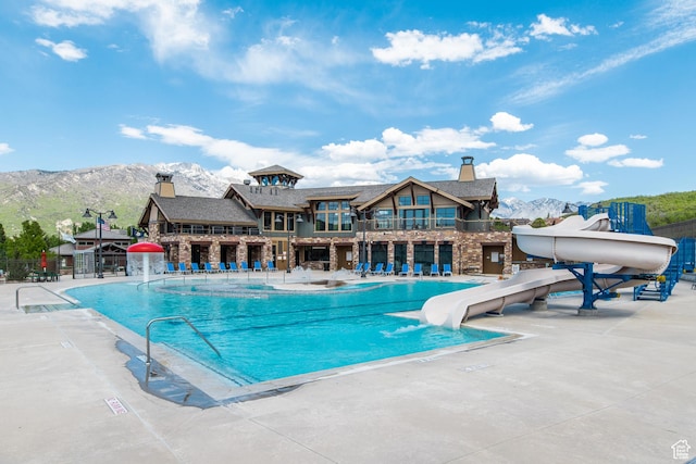 community pool with a water slide, a mountain view, fence, and a patio area
