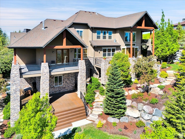 back of property with a balcony, stone siding, stucco siding, and stairway