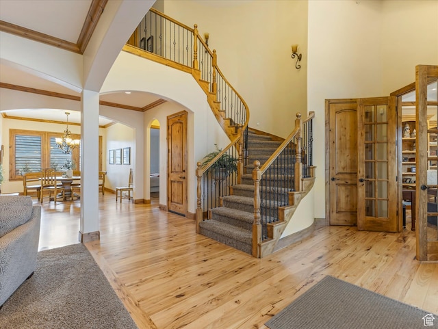 stairs featuring ornamental molding, hardwood / wood-style flooring, a towering ceiling, arched walkways, and a chandelier