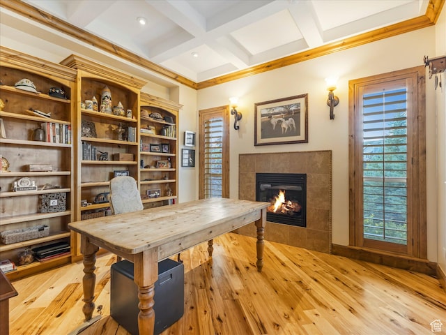 home office featuring a tiled fireplace, light wood-style flooring, coffered ceiling, and beamed ceiling