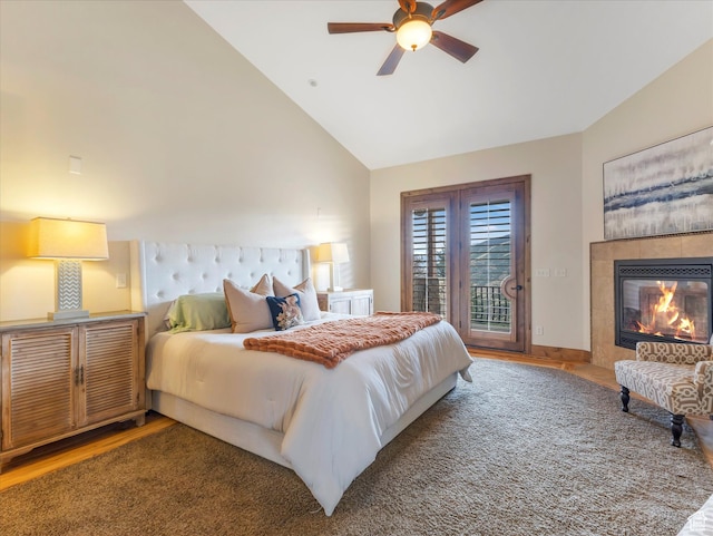 bedroom featuring access to outside, wood finished floors, a fireplace, a ceiling fan, and high vaulted ceiling