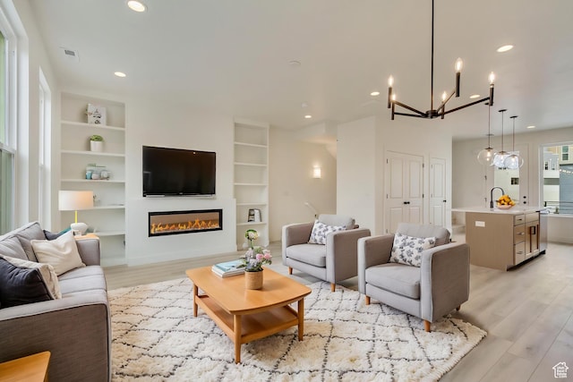 10641 S Pipestone Way Unit 139, South Jordan, UT 84009 - living room featuring light wood finished floors, a glass covered fireplace, built in shelves, a chandelier, and recessed lighting