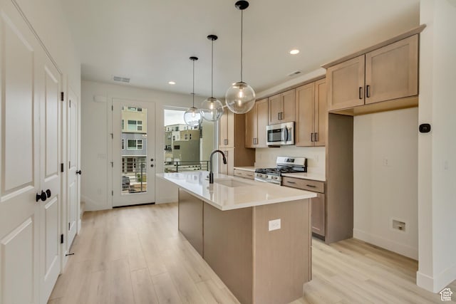 kitchen featuring appliances with stainless steel finishes, a sink, light wood-style flooring, a center island with sink, and recessed lighting