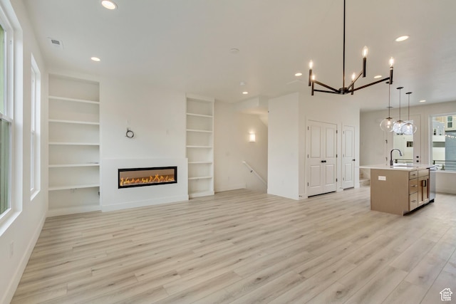 unfurnished living room featuring a sink, light wood-style floors, built in features, recessed lighting, and a chandelier