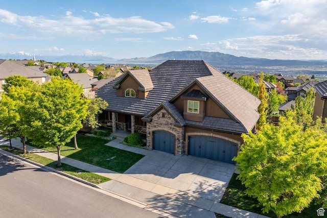 view of front of home with stone siding, driveway, a mountain view, and a front yard