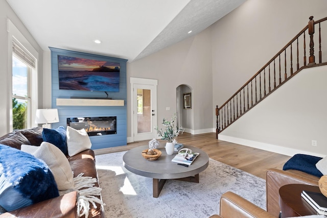 living area featuring arched walkways, vaulted ceiling, wood finished floors, baseboards, and stairway