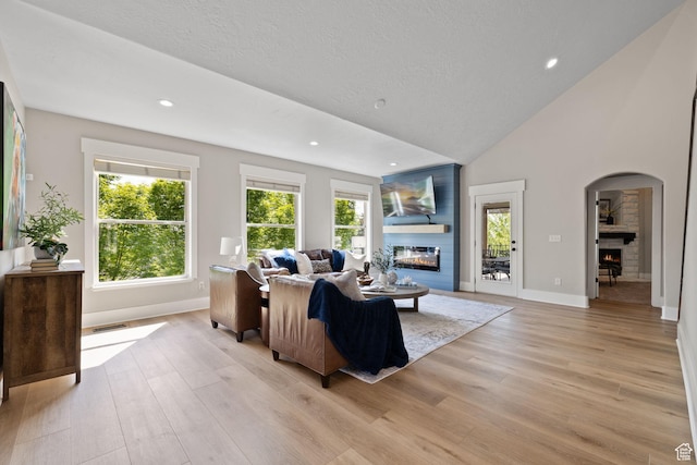 living area with a glass covered fireplace, light wood finished floors, arched walkways, recessed lighting, and high vaulted ceiling