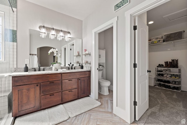 full bath with toilet, double vanity, and a spacious closet