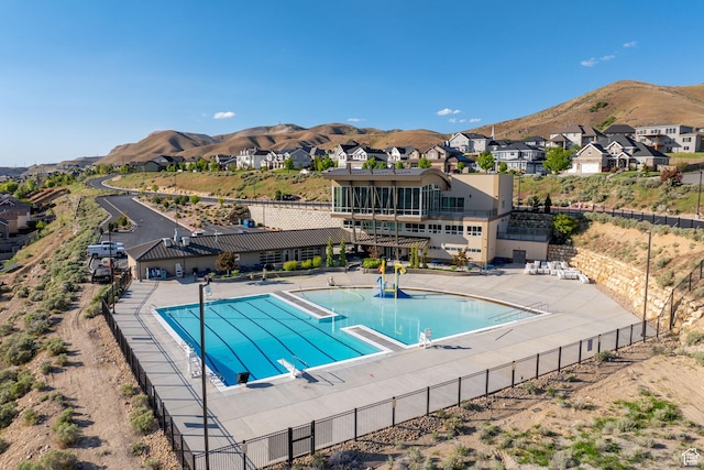 community pool with fence, a mountain view, a residential view, and a patio area