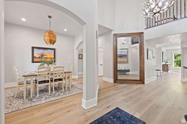 dining area with arched walkways, light wood-style flooring, baseboards, a chandelier, and a towering ceiling