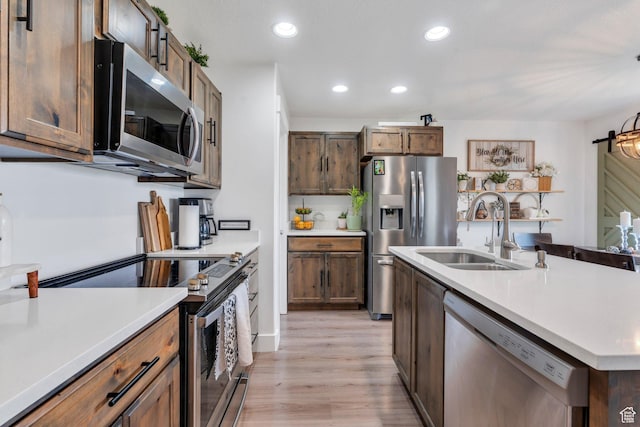 kitchen with stainless steel appliances, a sink, recessed lighting, light countertops, and light wood finished floors