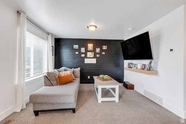 carpeted living room featuring an accent wall and baseboards