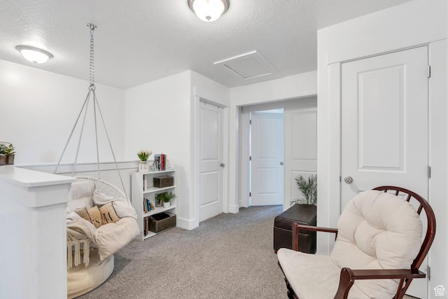 sitting room with attic access, a textured ceiling, and carpet floors